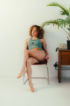 Woman sitting on a chair wearing a green pole wear set in a minimalistic room.